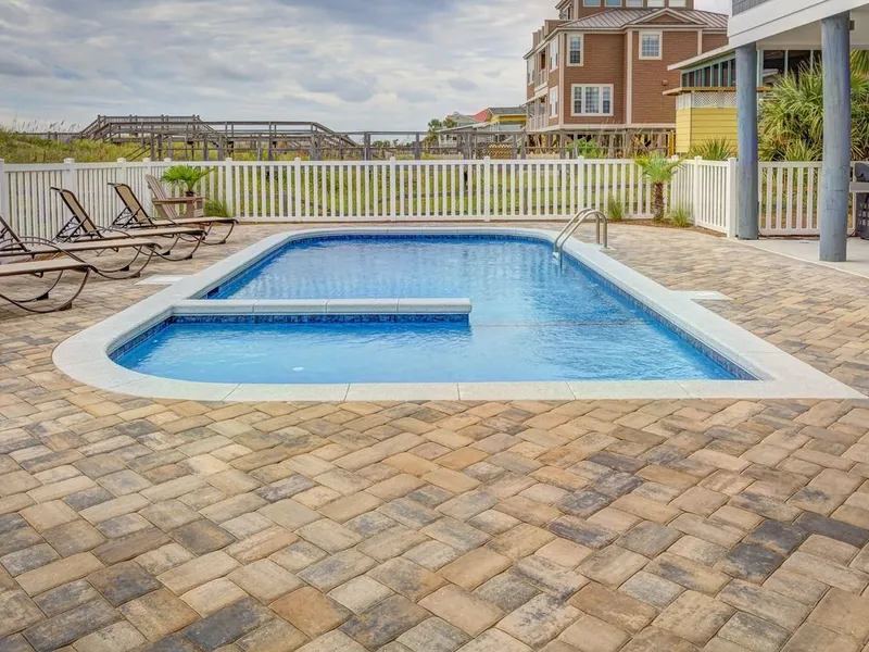 Pool deck with pavers beside a backyard swimming pool